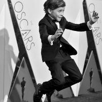 a young boy in a tuxedo jumps on the red carpet at an oscars event