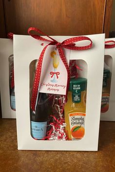 two bottles of orange juice in a white gift bag with red ribbon on the top