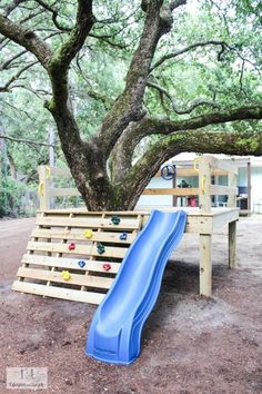 a blue slide sitting under a tree next to a wooden bench and swing set with balls on it