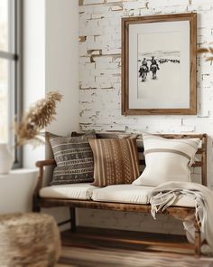 a wooden bench with pillows on it in front of a white brick wall and window