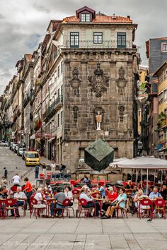 many people are sitting at tables in the middle of an old town square with tall buildings