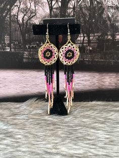 a pair of pink and black beaded earrings hanging from a stand on a snowy surface