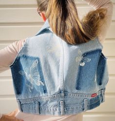 a woman wearing a jean vest with butterflies on the front and back, in front of a white wall