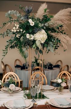 a tall centerpiece with white flowers and greenery sits on top of a table