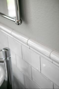 a bathroom with white tile and stainless steel faucet, toilet paper dispenser and sink