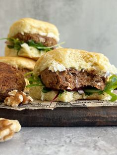 two burgers with meat, lettuce and feta cheese on a cutting board