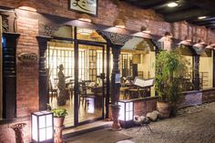 the entrance to a restaurant at night with lights on and potted plants in front