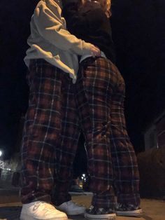 two people standing next to each other in plaid pants and white converse shoes at night