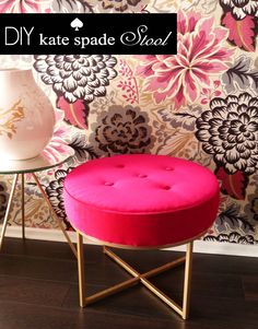 a pink ottoman sitting on top of a wooden floor next to a vase and wallpaper