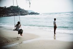 two people standing on the beach and one is swinging