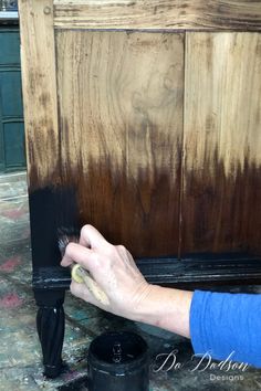 a person is painting the side of a wooden cabinet with brown and black paint on it