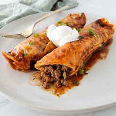 two enchiladas on a plate with sour cream