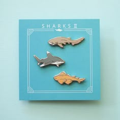 three shark and dolphin enamel pins on a blue card with the words sharks in white lettering