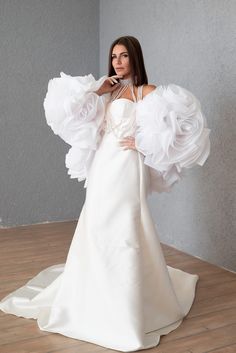 a woman in a white wedding dress with large ruffles on her arms and shoulders