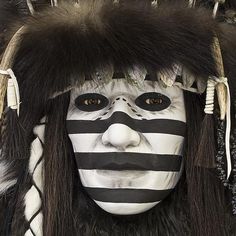 a man with white face paint and black hair wearing a striped headdress while standing in front of a mirror