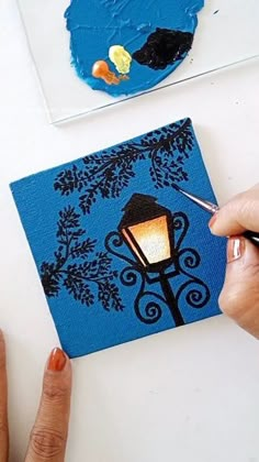 someone is painting on a piece of blue paper with a lamp post in the background