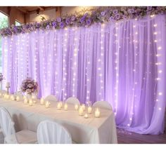 a long table with white chairs and purple drapes on the wall, decorated with candles