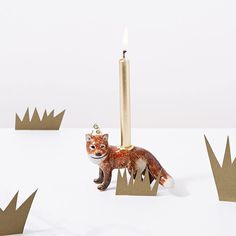 a candle with a fox figurine next to it on top of paper crowns