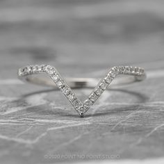 a white gold chevron ring with diamonds in the middle on top of a rock