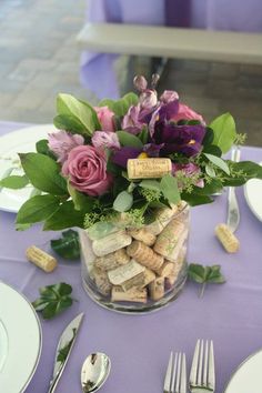 a vase filled with flowers and wine corks on top of a purple table cloth