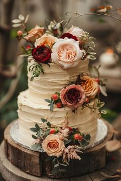 a three tiered wedding cake with white frosting and red flowers on top is sitting on a wooden stand