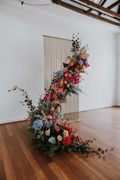 an arrangement of flowers is on the floor in front of a white wall and wooden floors