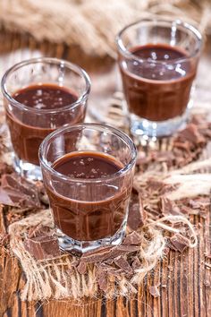 three glasses filled with chocolate pudding on top of a wooden table