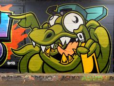 graffiti on the side of a building with a large green alligator biting it's teeth