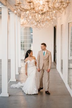 a bride and groom holding hands walking down the aisle in front of a chandelier