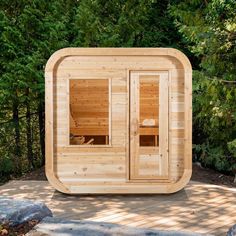 a wooden sauna in the middle of a wooded area with doors open and two people inside