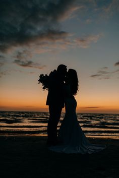 a bride and groom kissing on the beach at sunset