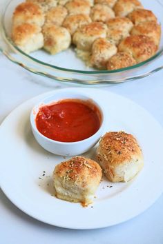 two small rolls on a plate next to a bowl of tomato sauce and some bread