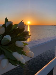 the sun is setting over the ocean with white tulips