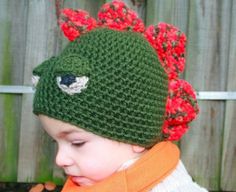 a small child wearing a green crocheted hat with red flowers on it's brim