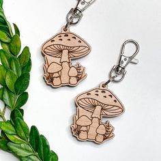 two wooden keychains with mushrooms on them sitting next to some green leafy branches