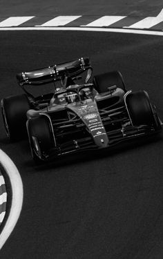 a black and white photo of a race car driving on a track with the driver behind it