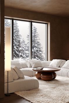 a living room with large windows and white furniture in front of the snow covered trees