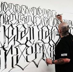 a man is writing on a wall with black and white letters in front of him