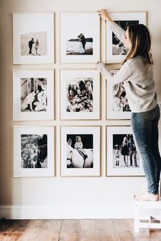 a woman standing on a stool in front of a wall with pictures hanging on it