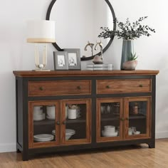 a wooden cabinet with glass doors and drawers in front of a round mirror on the wall