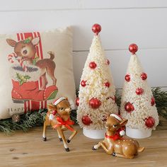 three small christmas trees sitting next to each other on a wooden table with two deer figurines