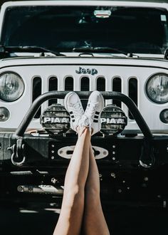 a woman's legs hanging over the front bumper of a white jeep