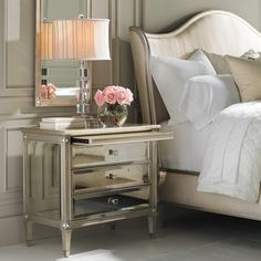 a white bed sitting next to a mirror and lamp on top of a wooden table