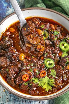 a spoon full of chili beef stew with peppers and jalapenos