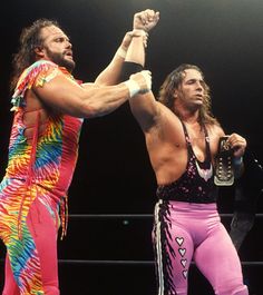 two men standing next to each other on top of a wrestling ring with their fists raised