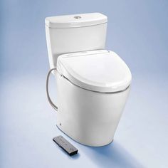 a white toilet sitting next to a remote control on a blue surface with a light blue background