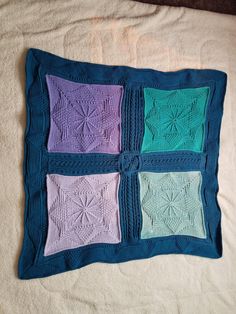 a blanket that has four squares on it, each with different colored crochets