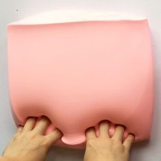 two hands are holding the back of a pink object that looks like it is floating on water