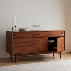 a wooden cabinet with two wine glasses on top and plates in the bottom, next to a white rug