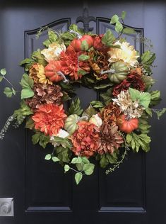 a black door with a wreath on it that has orange and yellow flowers in the center